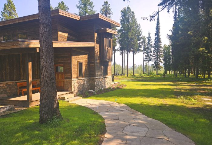 Flagstone walkway through a landscaped lawn leading to a modern wood and stone residence, by Beargrass Landscape Architecture in Flathead County MT
