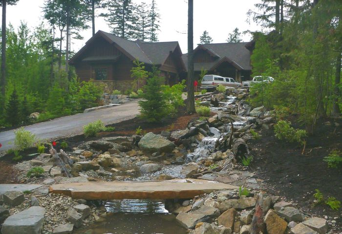 Constructed stream feature with rock lining and a wood plank crossing alongside the driveway, finished landscape design by Beargrass Landscape Architecture