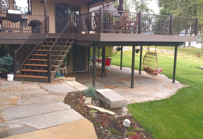 Steps from the main floor down to a flagstone patio and landscaped ground-level seating area, a Whitefish Lake shoreline project by Beargrass Landscape Architecture
